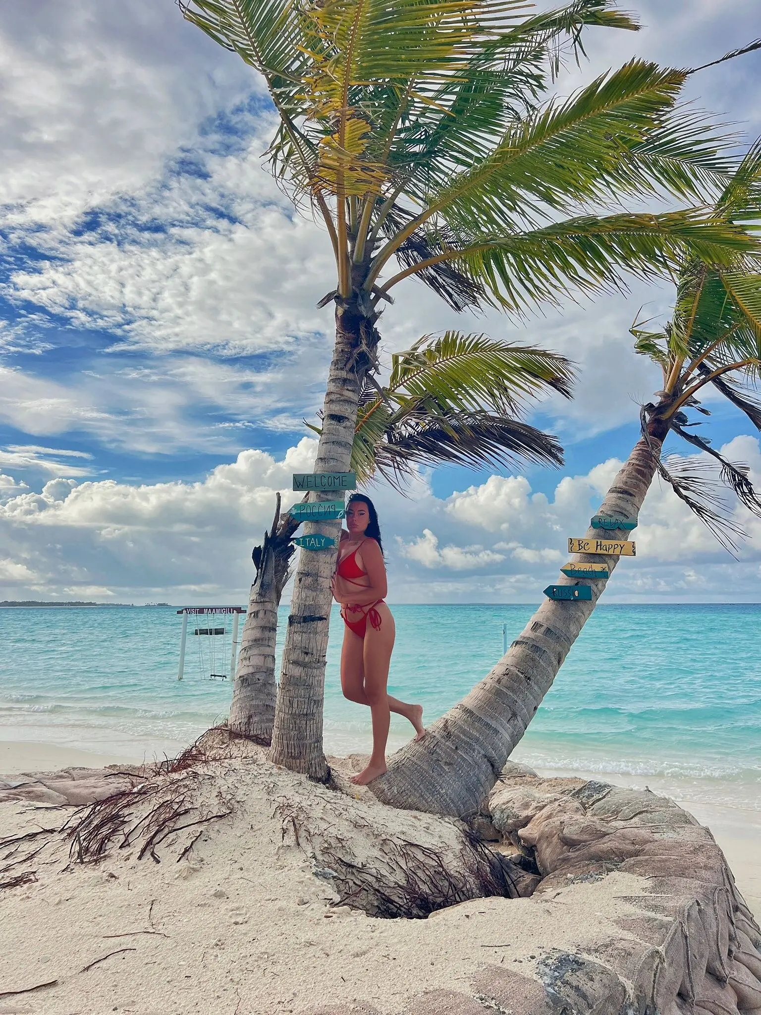 Guest beside a leaning palm on Maamigili's white-sand beach over turquoise water