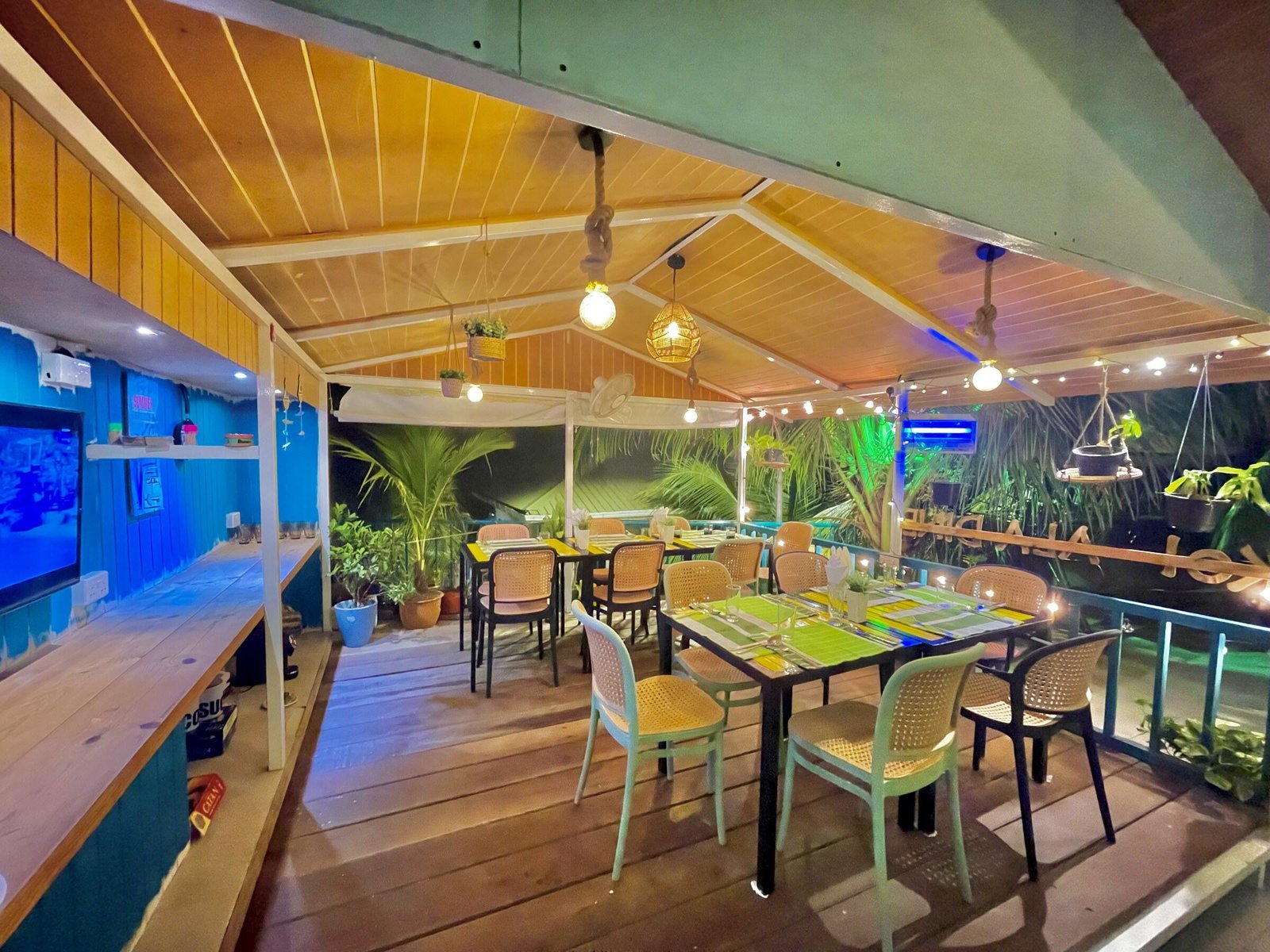 Koimala's open-air restaurant lit for the evening, with timber ceiling, plants and an aquarium wall on Maamigili