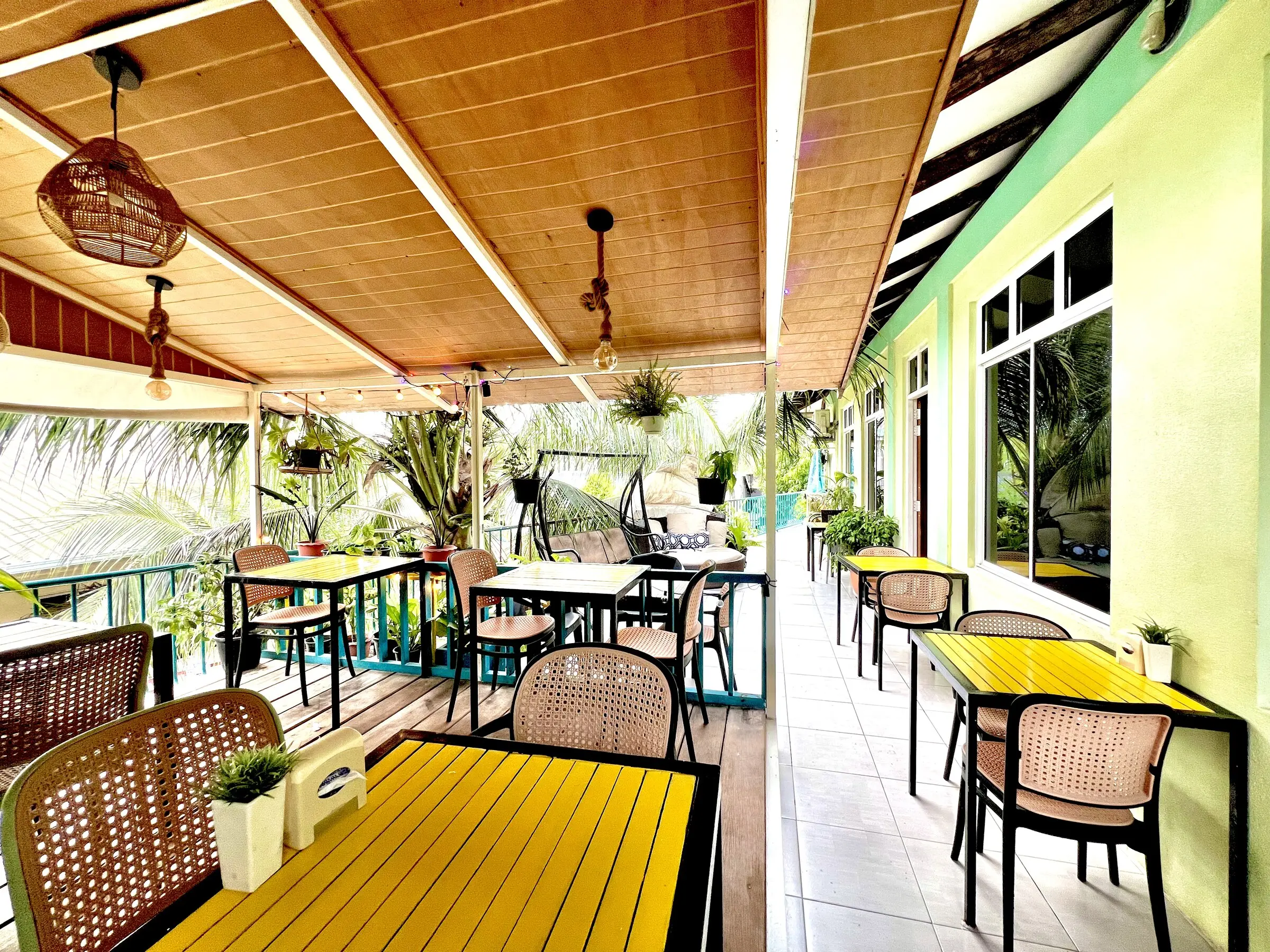 Open-air dining terrace with a timber ceiling, yellow tables and palms at Koimala Maamigili